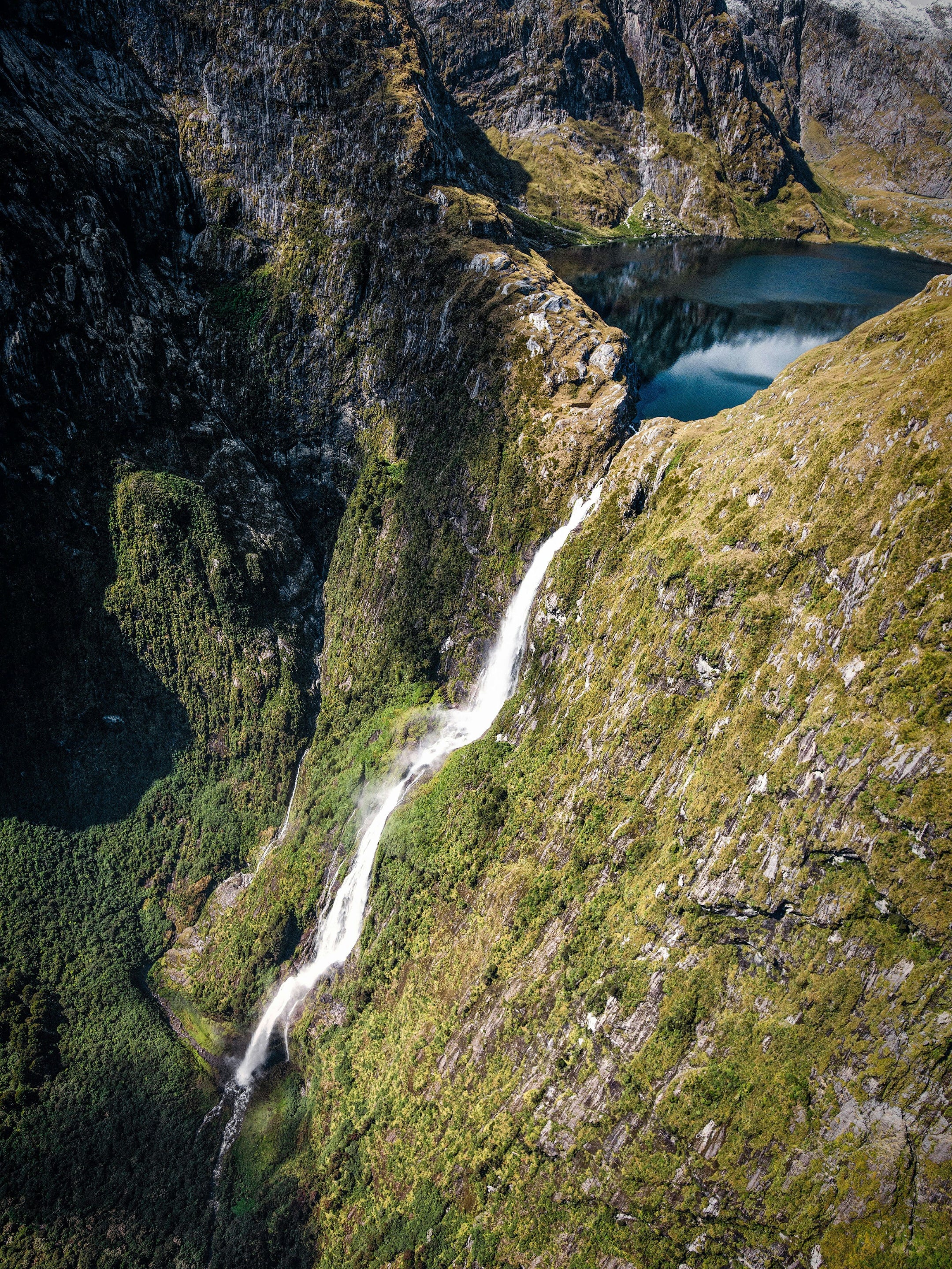Mountainous landscape with a waterfall pouring out of a lake down a cliff in New Zealand.