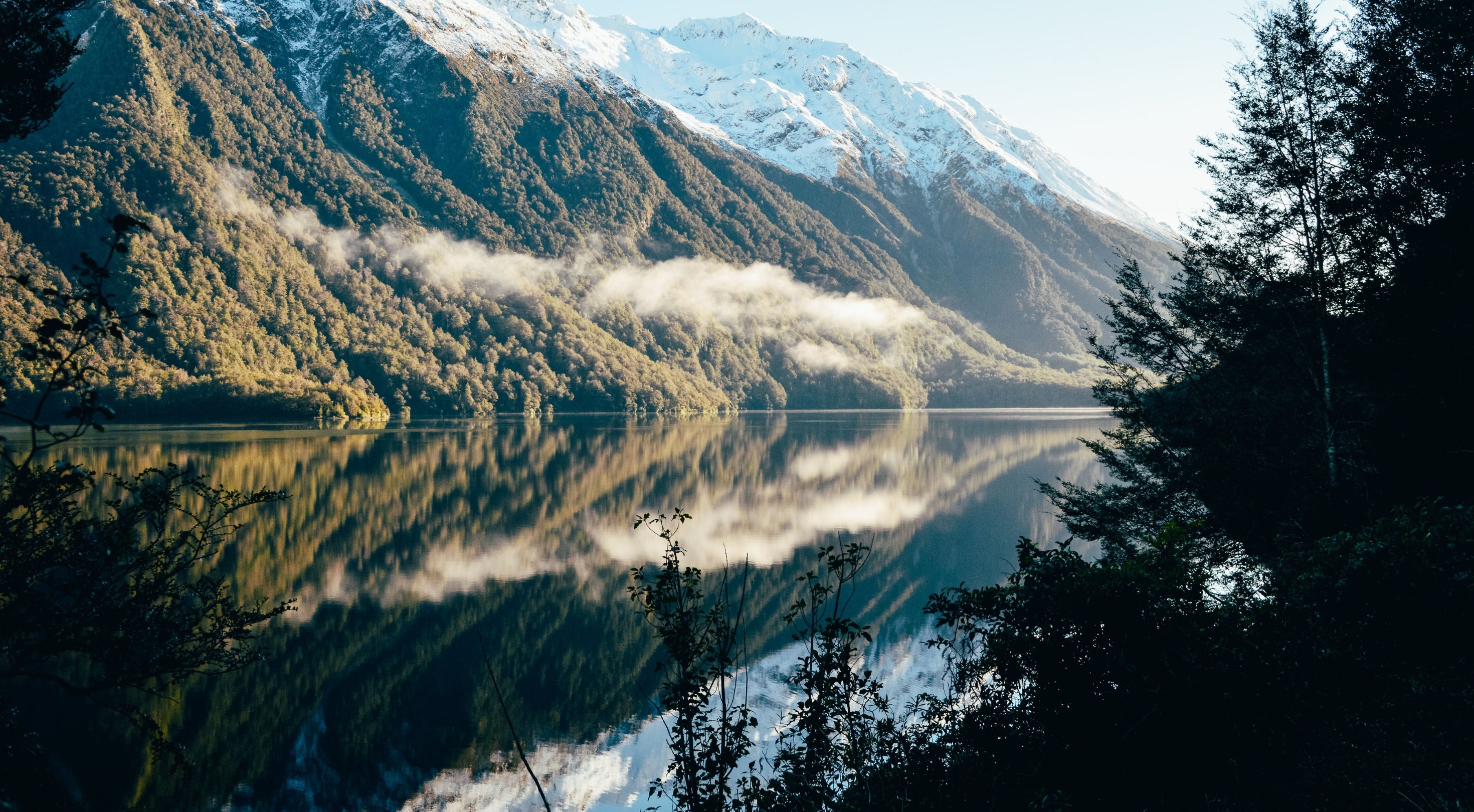 Mountainous landscape with a lake and reflection, surrounded by native New Zealand bush.