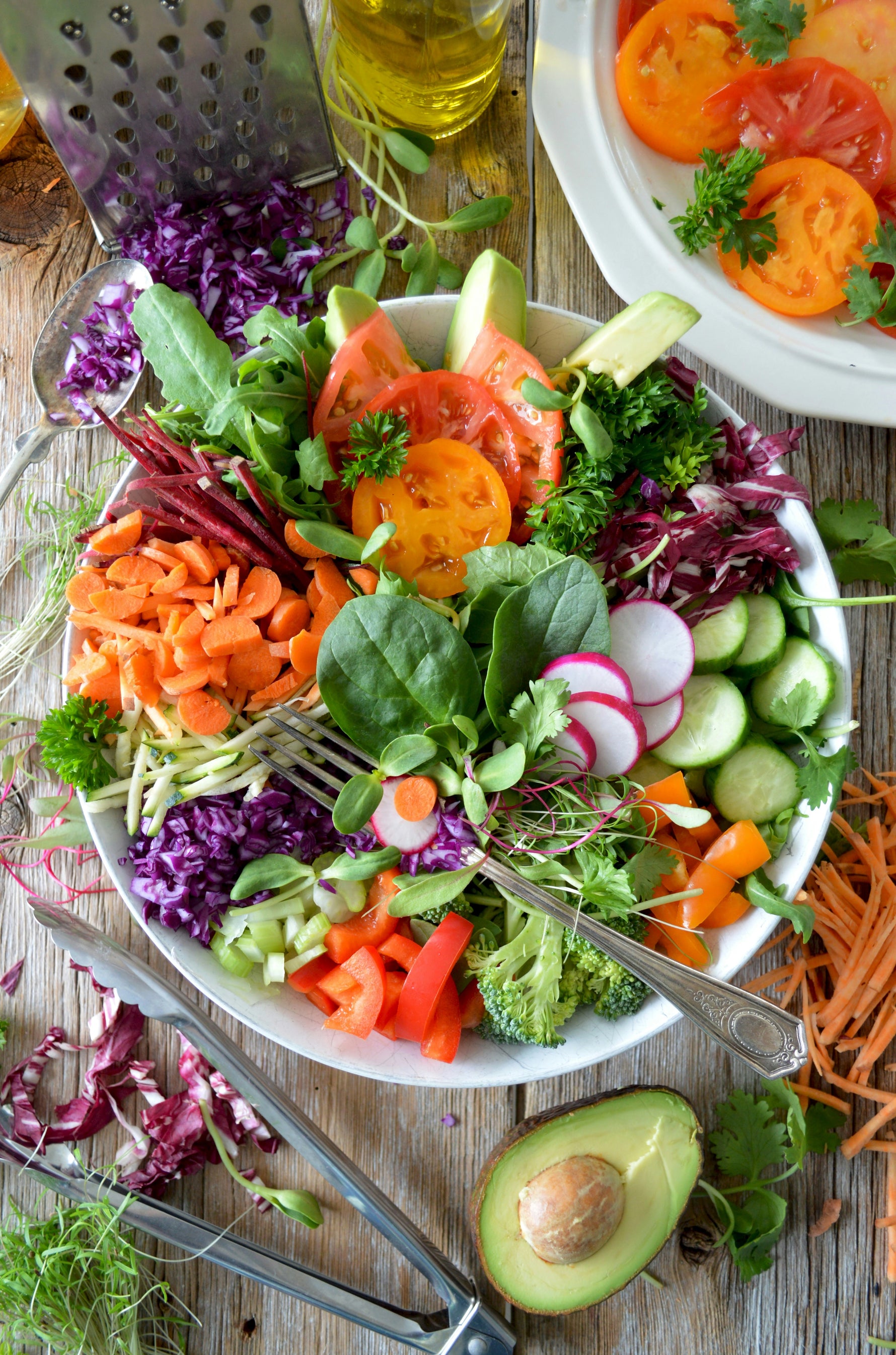 Assorted fresh vegetables on a plate with a fork, including carrots, tomatoes, and avocado, on a wooden surface.