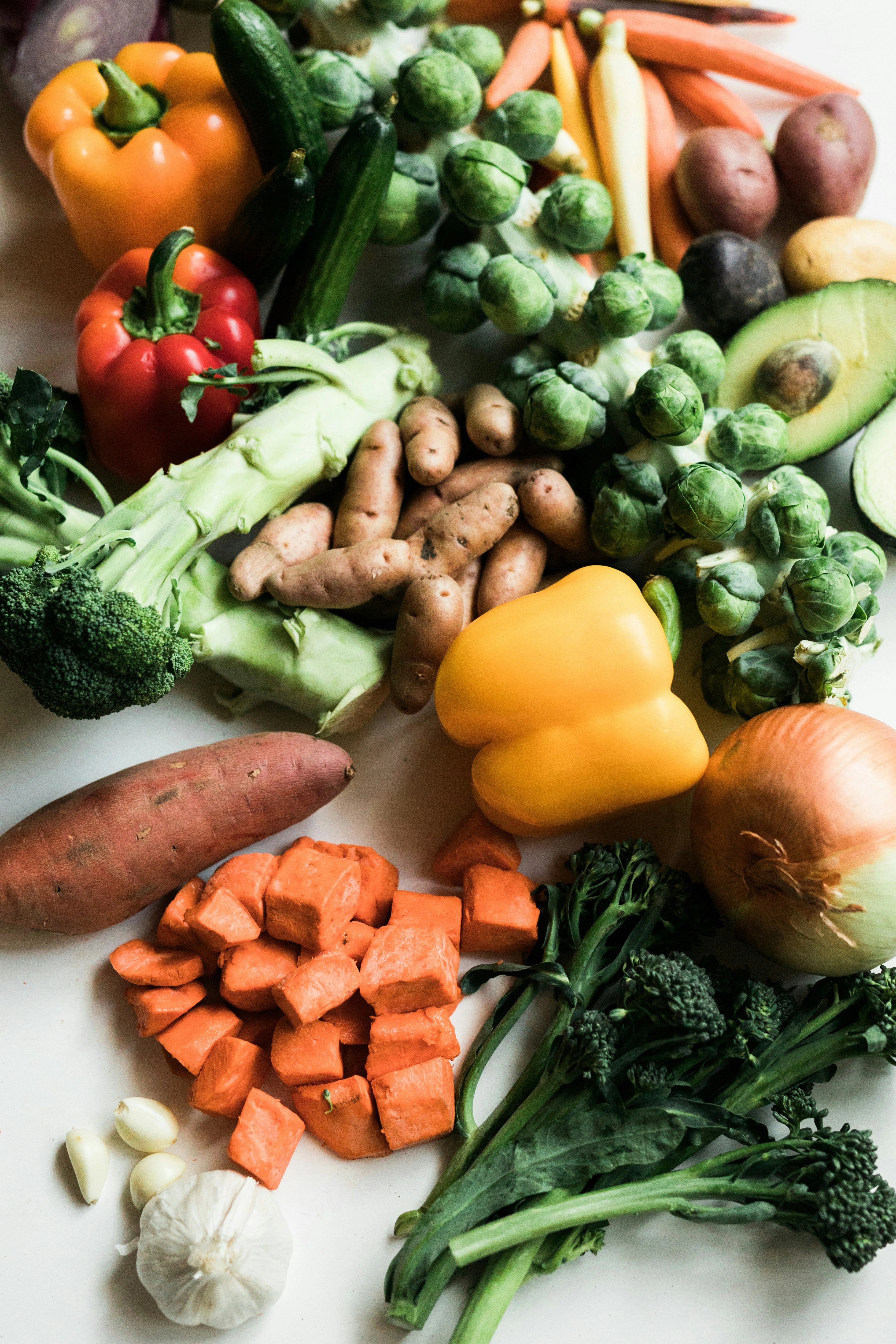 Assorted fresh vegetables including carrots, broccoli, bell peppers, and potatoes on a white surface.